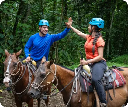 Two travelers horseback riding through a tropical rainforest trail near La Fortuna Waterfall in Costa Rica with a local guide.